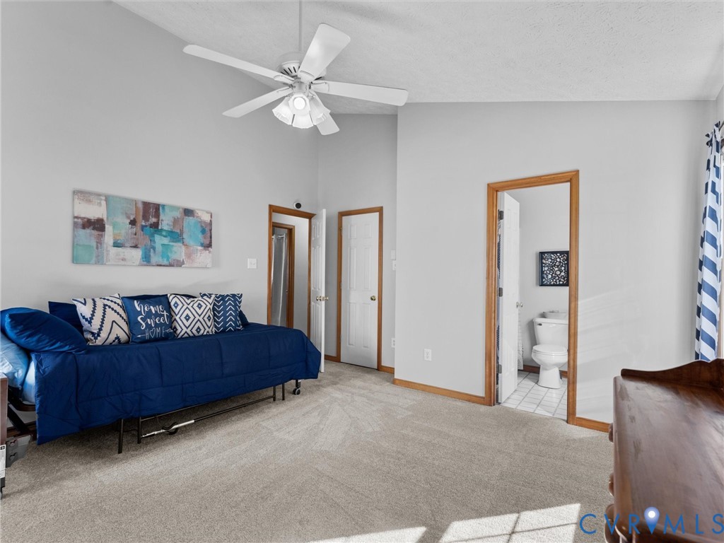 Vaulted ceiling with central light fixture and ceiling fan, neutral carpeting, and wood-trim door frames