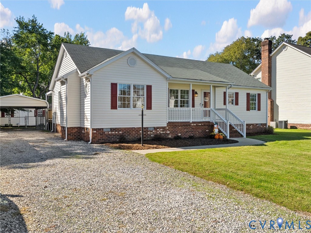 Single-story exterior featuring a brick foundation, horizontal siding, shutter accents, a front porch with white railing, and a detached carport