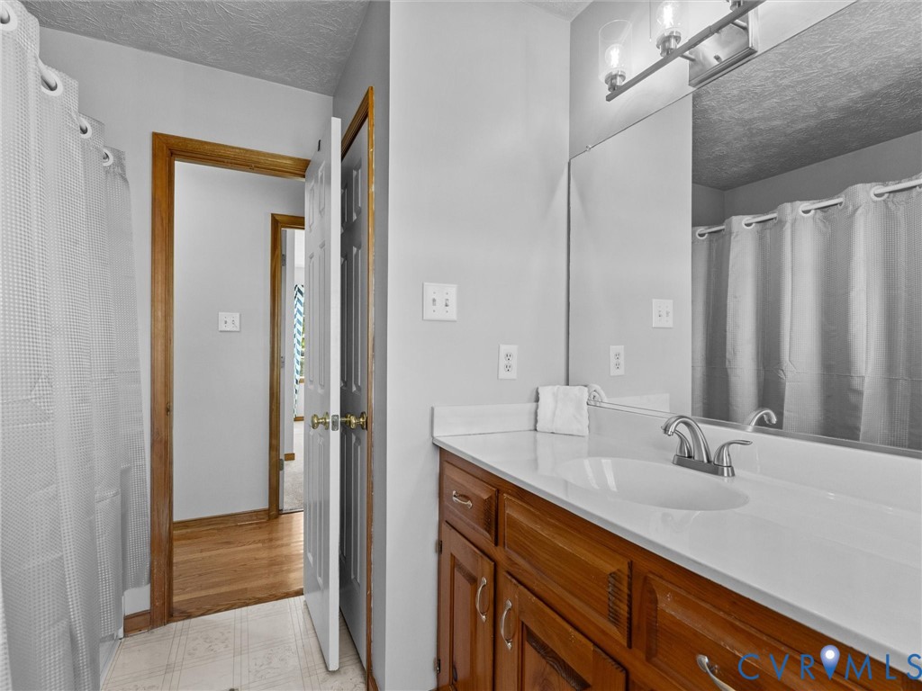 Bathroom featuring a vanity with wood-finish cabinetry, an integrated sink with a chrome dual-handle faucet, a full-width mirror, and a wall-mounted light fixture