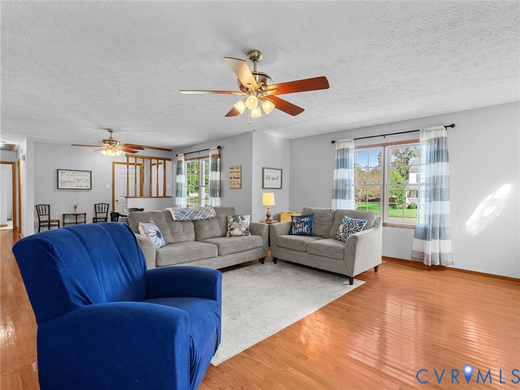 Living space featuring wood-finish flooring, dual ceiling fans with integrated lighting, and multiple windows