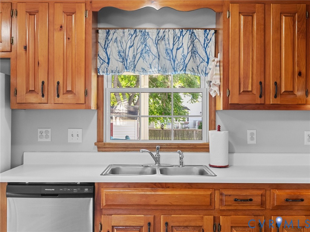 Natural wood cabinetry, white solid-surface countertops, dual-basin stainless steel sink with chrome faucet, and multi-pane window