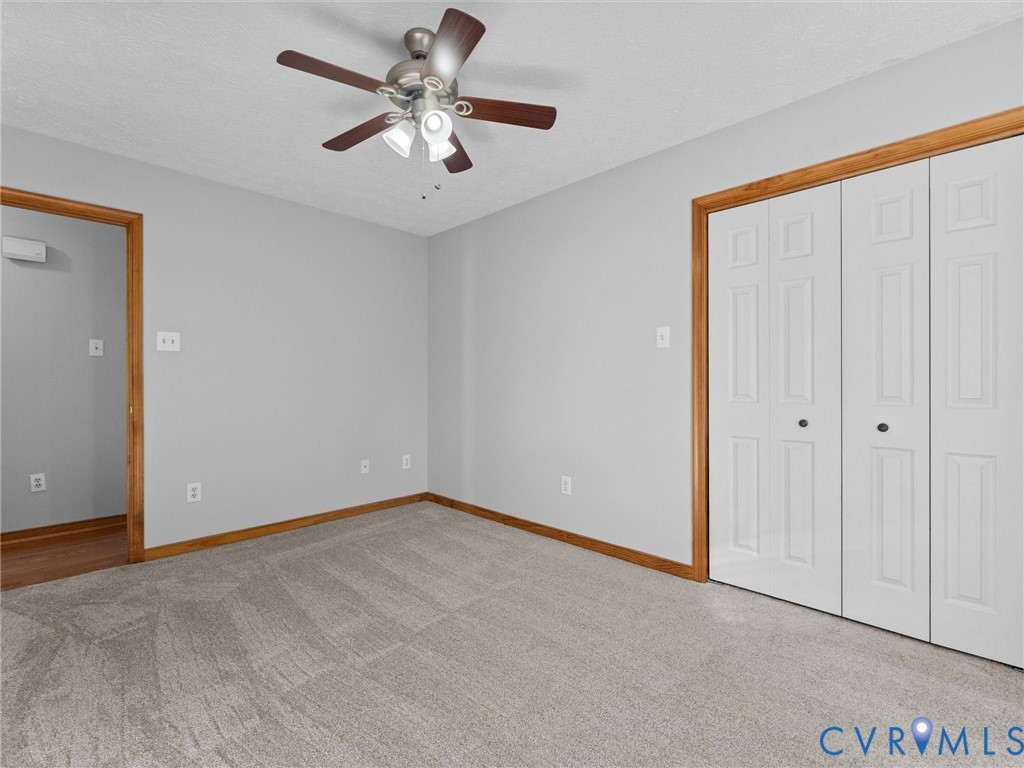 Room interior featuring neutral wall paint, carpeted flooring, a ceiling fan with integrated lighting, and white bifold closet doors with wood trim finish
