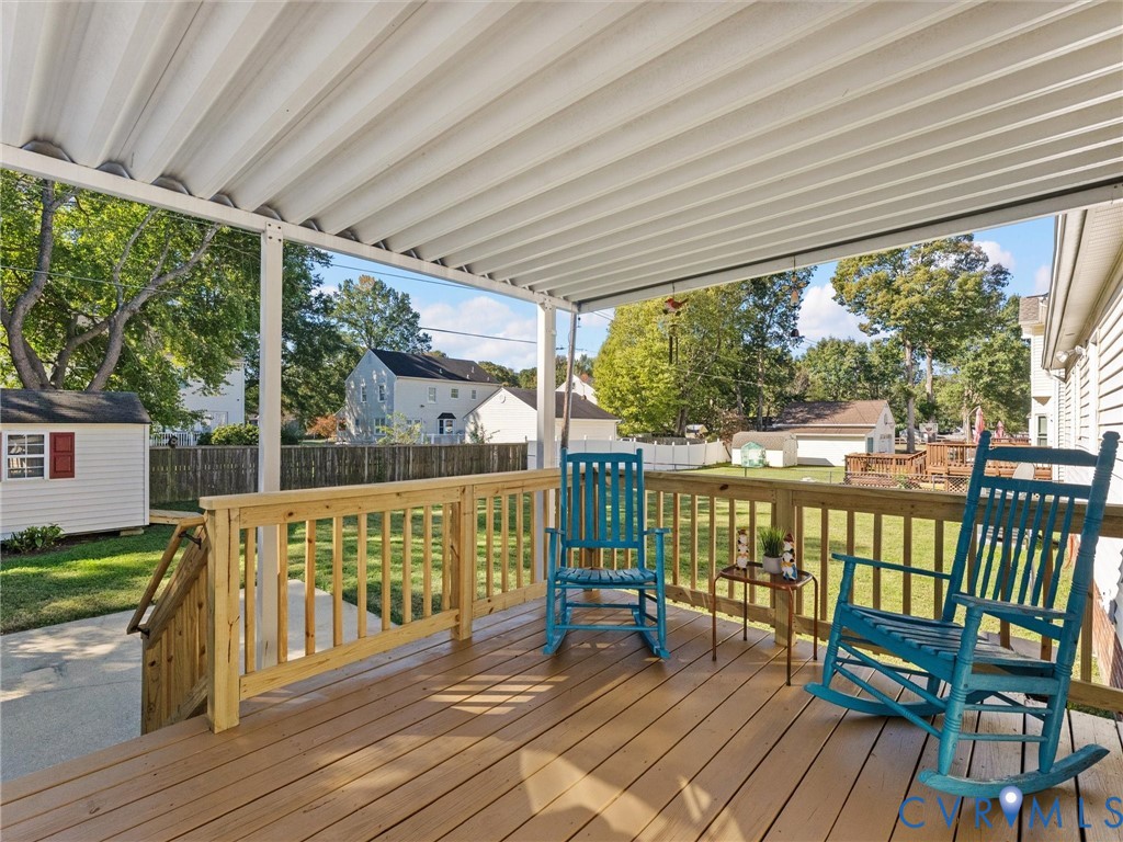 Elevated deck featuring wood-finish decking, a wooden railing, and a corrugated metal patio cover