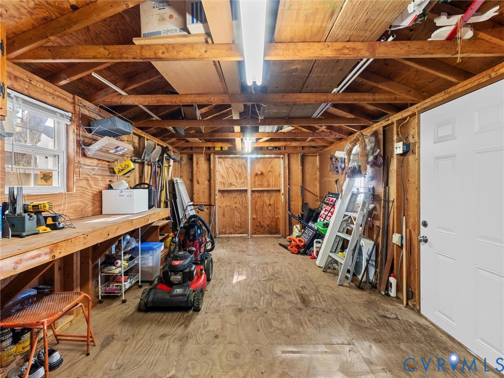Outbuilding featuring wood-paneled walls, exposed rafter ceiling, built-in workbench, double-door entry, and linear fluorescent lighting