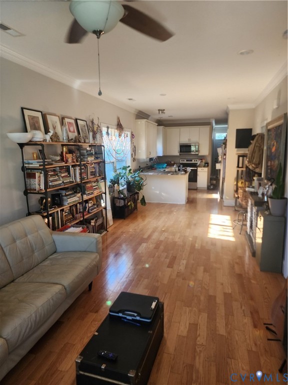 Open-concept space featuring wood-finish flooring, recessed lighting, crown molding, and kitchen cabinetry with integrated microwave and oven