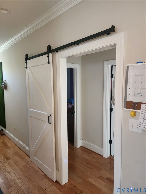 White sliding barn door featuring a matte black track and hardware, complemented by wood-finish flooring and crown molding