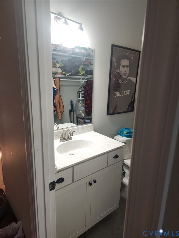 Vanity featuring a white cabinet base, stone-composite countertop with an integrated oval sink, polished metal faucet, and wall-mounted vanity lighting