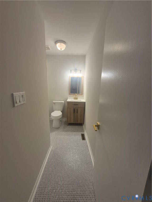 Restroom featuring penny tile flooring, a wood-finish vanity with a stone countertop, a brass-tone faucet, and a wall-mounted vanity light