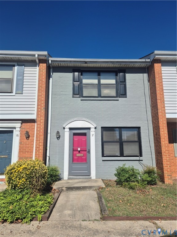 Painted brick facade featuring a decorative arched doorway pediment, shuttered windows, and a concrete walkway