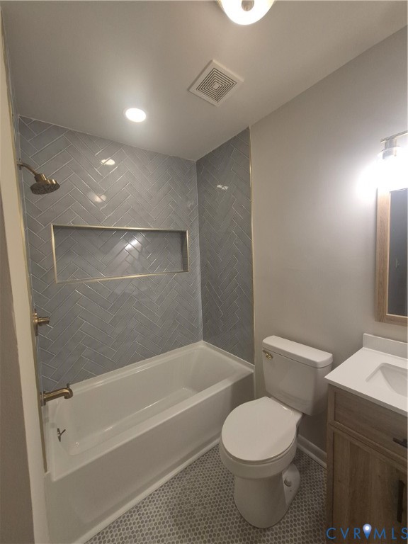 Full bathroom featuring herringbone-patterned wall tile, recessed shower niche, wood-finish vanity with white countertop, and hexagonal floor tiling