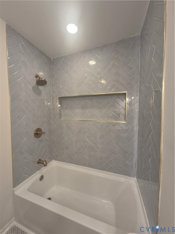 Bathtub enclosure featuring light gray herringbone-patterned wall tile, brass-finish fixtures, and a recessed tiled niche with brass-toned trim