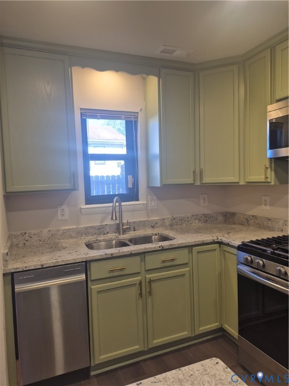 Kitchen featuring sage green shaker cabinetry, light-toned stone-finish countertops, stainless steel appliances, and a double-basin undermount sink with a high-arc pull-down faucet