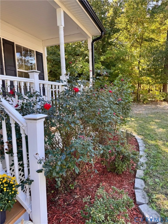Covered porch featuring white wooden railings, columns, and a landscaped garden bed with rose bushes, decorative mulch, and stone edging