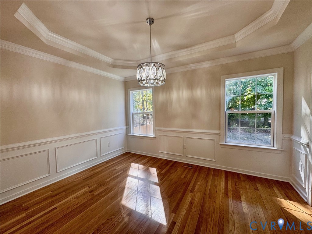 Tray ceiling with crown molding, wainscoting, wood-finish flooring, and a decorative pendant light fixture
