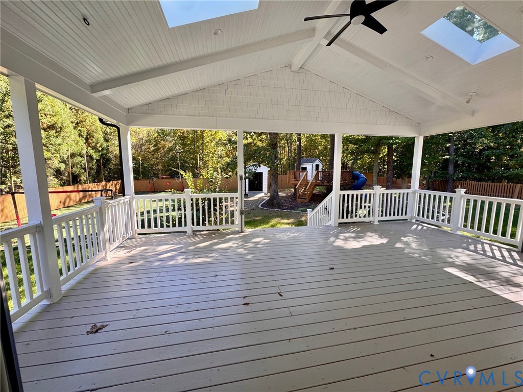 Covered deck featuring a vaulted tongue-and-groove ceiling, dual skylights, a ceiling fan, and white railing enclosures