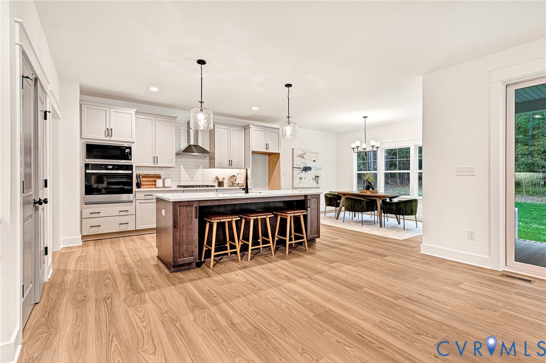 Kitchen featuring wood-finish flooring, a central island with a contrasting dark finish, white cabinetry, integrated stainless steel appliances, and glass pendant lighting