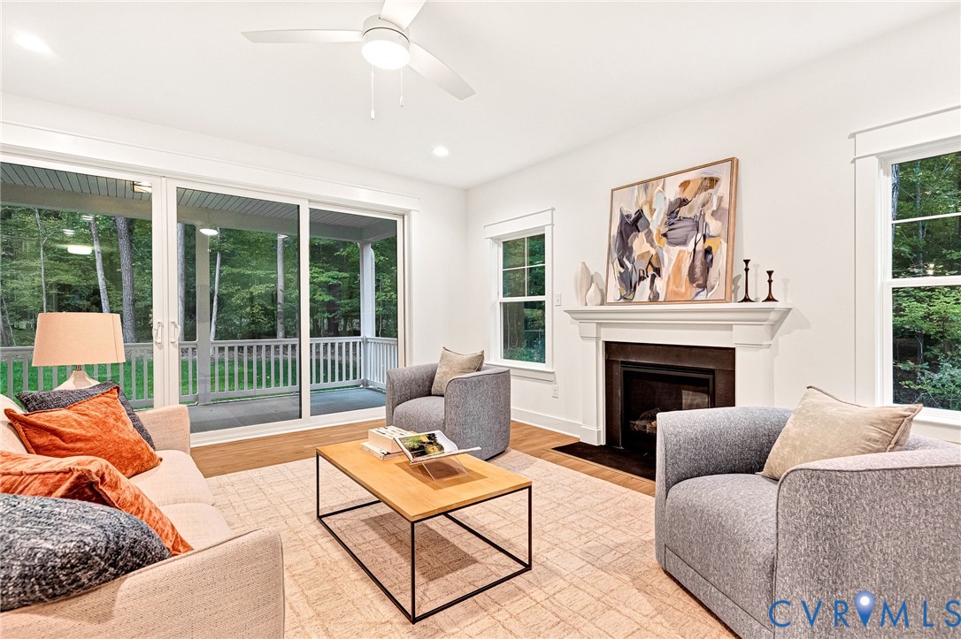 Living area featuring wood-finish flooring, a fireplace with a white mantel, sliding glass doors, and a ceiling fan