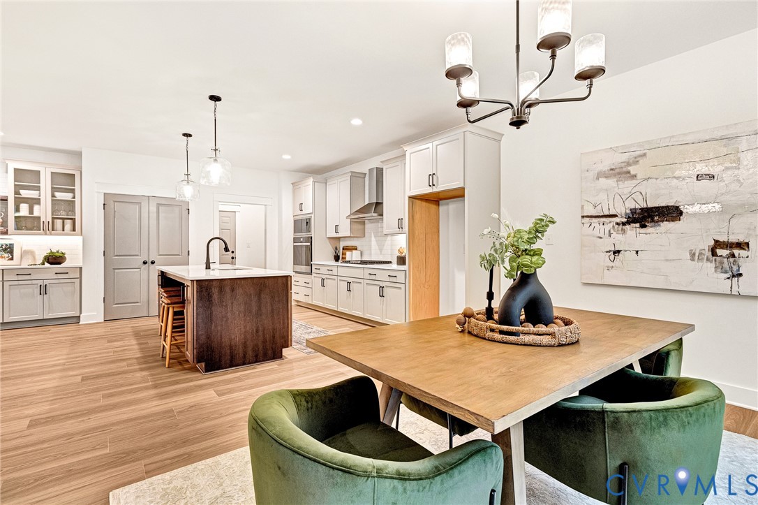 Kitchen featuring wood-finish flooring, a central island with a contrasting dark wood base and stone countertop, light-colored shaker-style cabinetry, a stainless steel wall oven, and a five-light chandelier