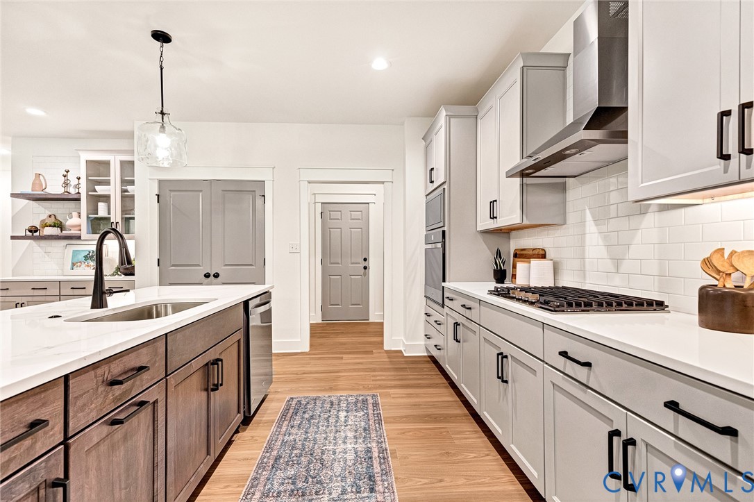 Kitchen featuring light-toned cabinetry, a central island with a stainless steel sink, solid-surface countertops, white tile backsplash, and wood-finish flooring