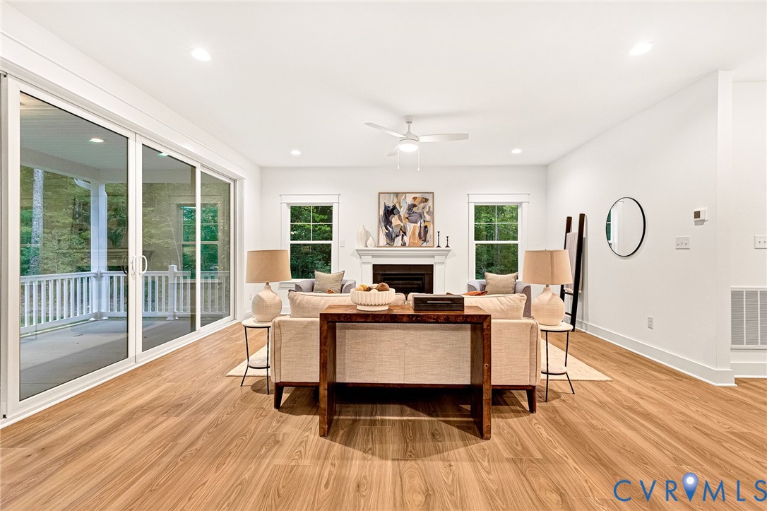 Living space featuring wood-finish flooring, a fireplace with a mantel, recessed lighting, a ceiling fan, and large sliding glass doors
