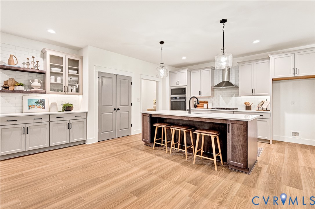 Kitchen featuring shaker-style cabinetry, a central island with countertop seating, stainless steel appliances, subway tile backsplash, and wood-finish flooring