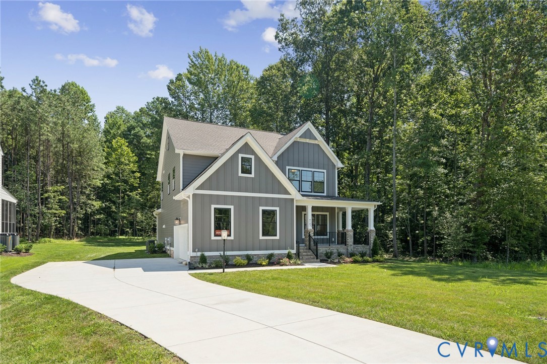 Two-story residence featuring vertical board-and-batten siding, a covered front porch with stone pillar accents, a multi-gabled roofline, and a concrete driveway