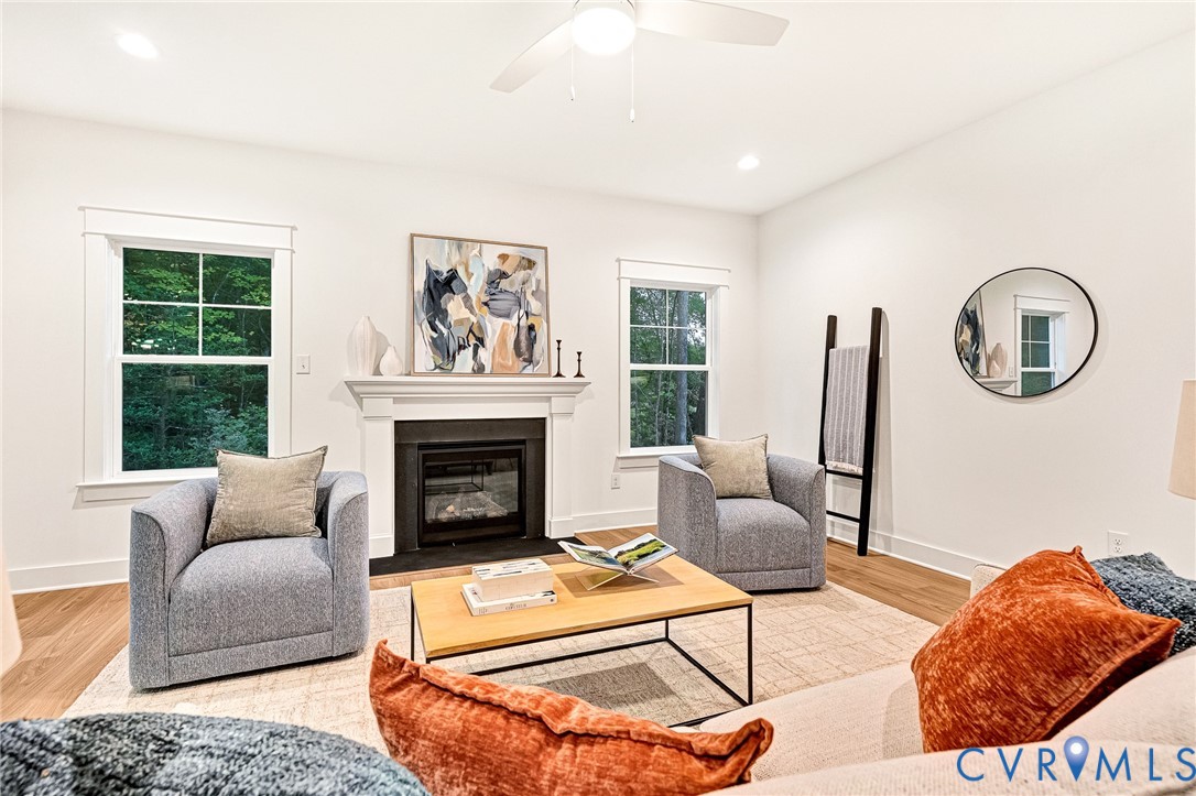Living area featuring a fireplace with a white mantel, wood-finish flooring, and white-framed windows