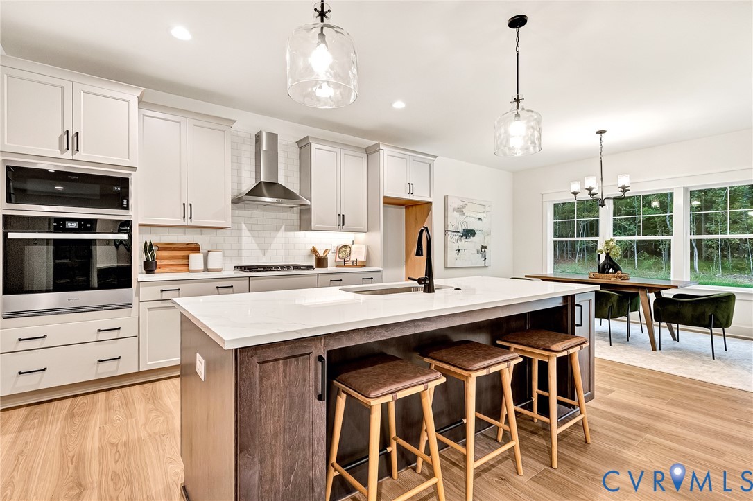 Kitchen featuring shaker-style cabinetry, a central island with a solid surface countertop, stainless steel built-in double ovens, a glass-tiled backsplash, and wood-finish flooring