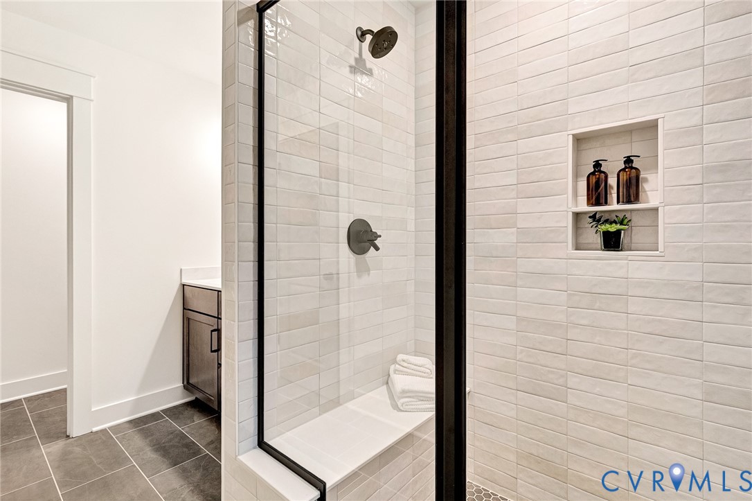 Walk-in shower featuring white subway-style wall tile, a built-in tiled bench, a recessed shower niche, and matte black fixtures, enclosed by a black-framed glass partition