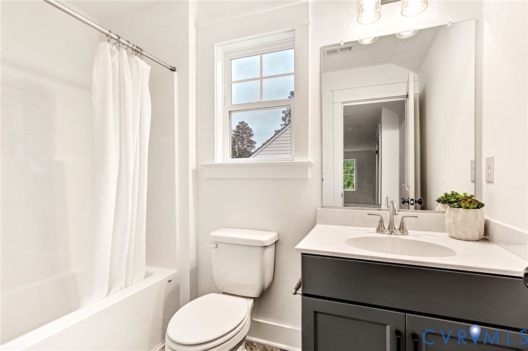 Bathroom featuring a dark-toned vanity with a light-colored countertop, integrated sink, large wall-mounted mirror, and a combination tub and shower with white surround