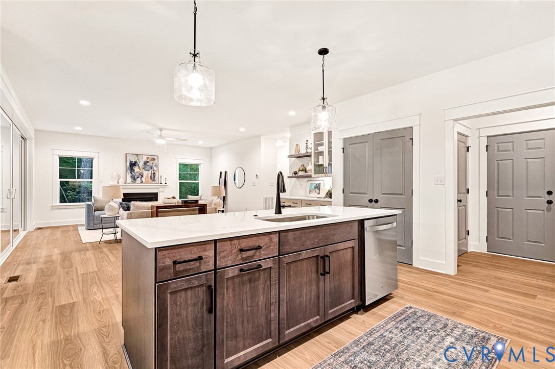 Kitchen island featuring a stone countertop, an undermount sink with a matte black faucet, wood-finish cabinetry, and dual glass pendant lights