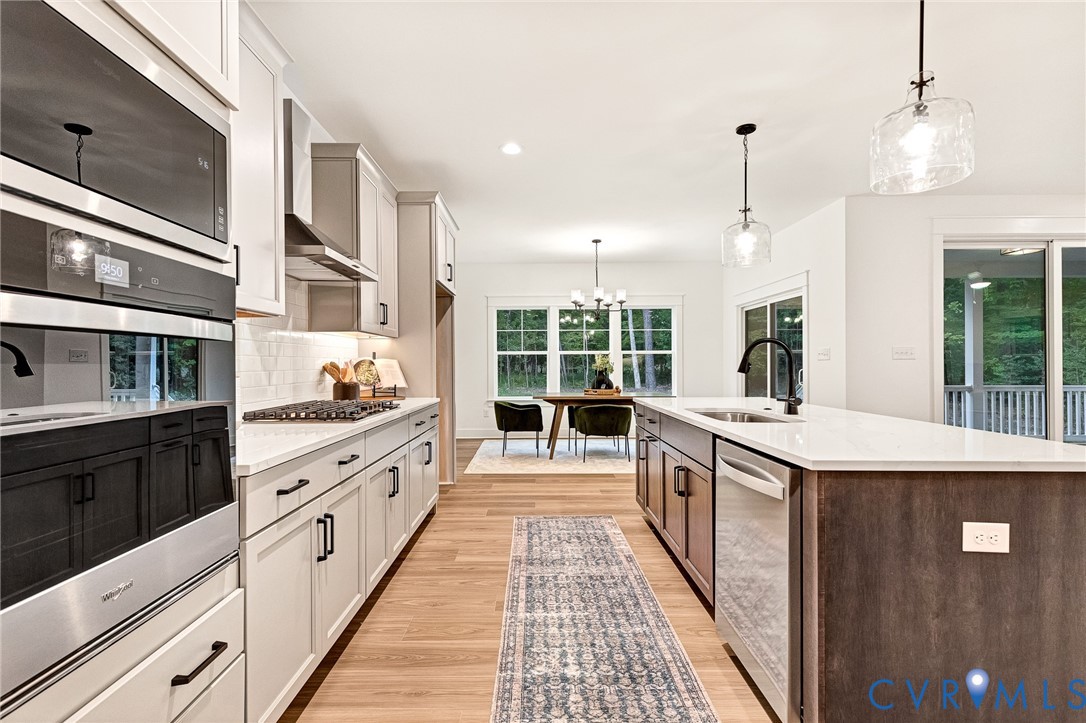 Kitchen featuring light-toned shaker cabinetry, a contrasting dark-finish kitchen island with a stone-surface countertop, built-in stainless steel double ovens, wood-finish flooring, and glass pendant lighting
