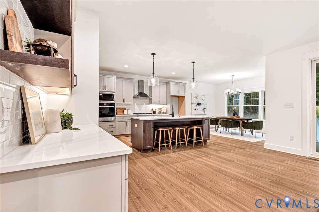 Kitchen featuring light cabinetry, a contrasting dark wood kitchen island, wood-finish flooring, white subway tile backsplash, and stainless steel built-in appliances