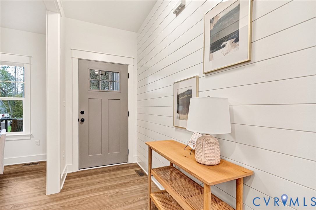 Entryway featuring white horizontal shiplap wall paneling, wood-finish flooring, and a grey Craftsman-style front door with a single-pane glass insert