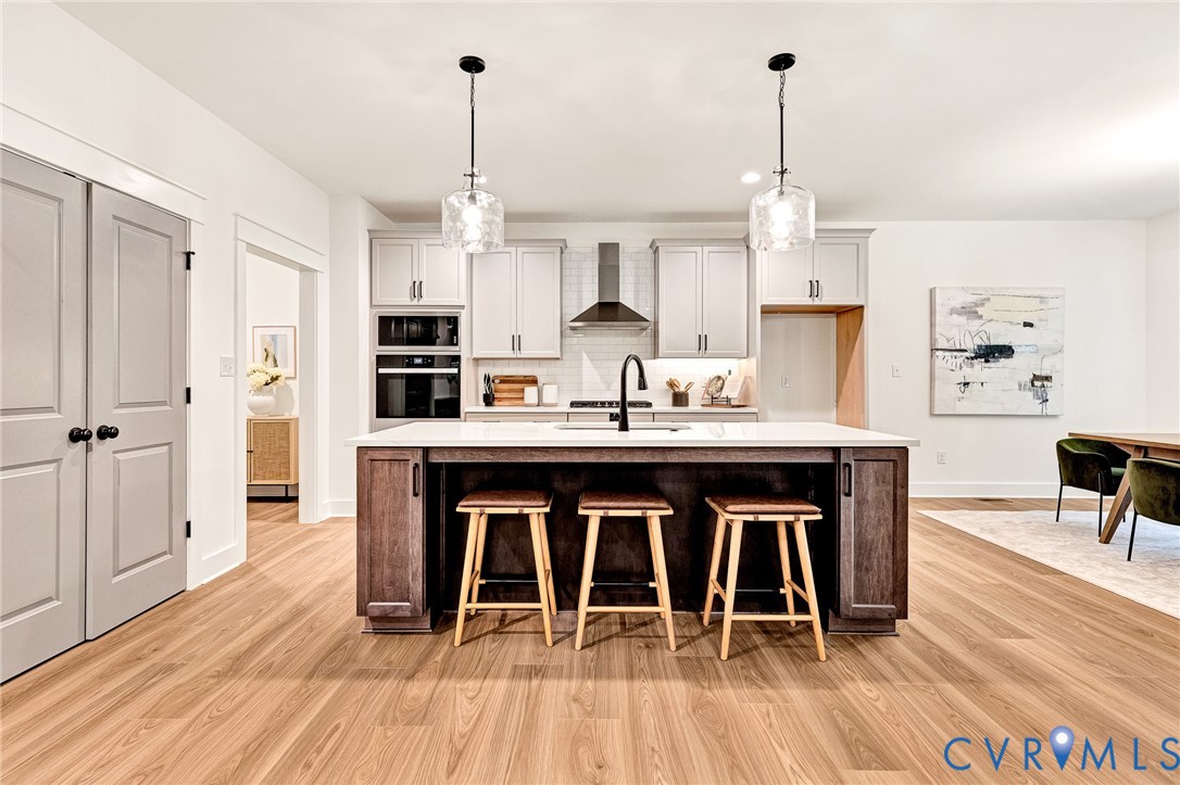 Kitchen featuring a center island with a stone-finish countertop, stainless steel wall-mounted oven and microwave, custom cabinetry, wood-finish flooring, and dual glass pendant light fixtures