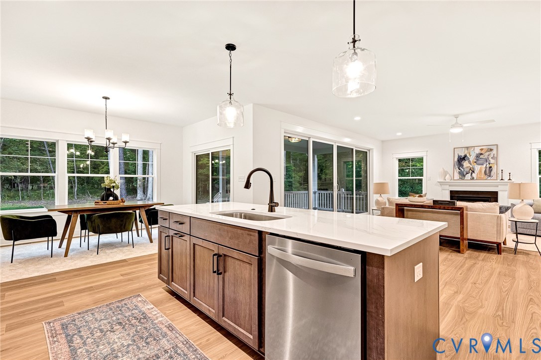 Kitchen island with stone-finish countertop, undermount sink, matte black faucet, and built-in stainless steel dishwasher, complemented by wood-finish flooring and pendant lighting