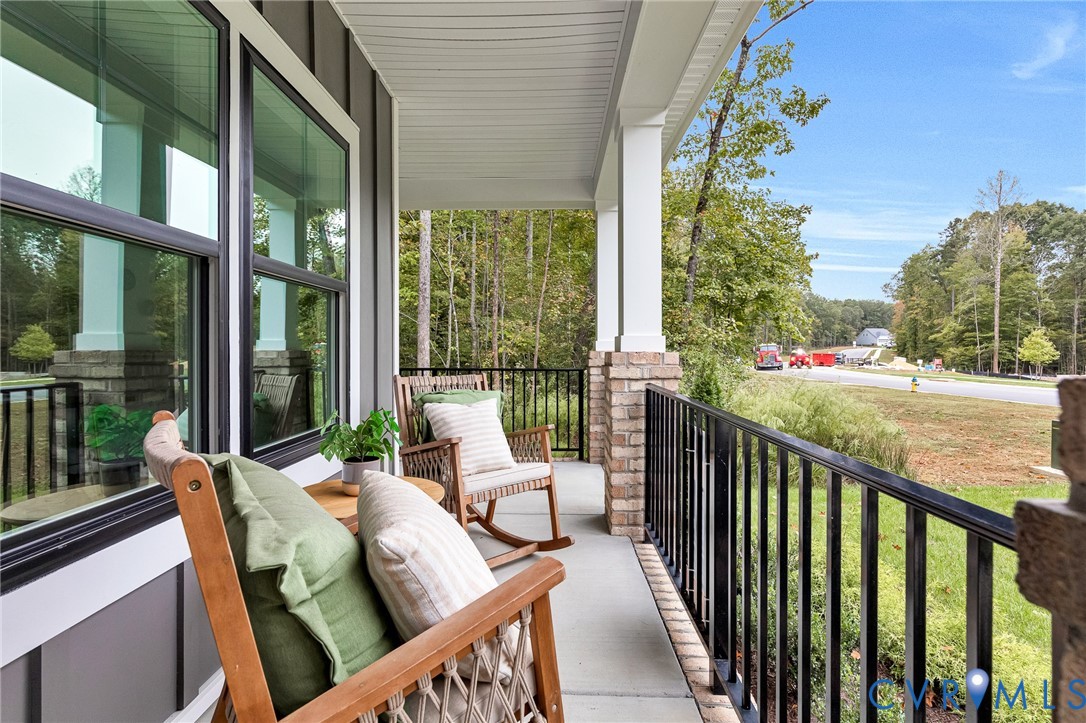 Covered porch featuring concrete flooring, black metal railing, and columns with brick masonry bases