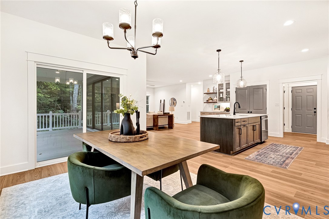Open-concept interior featuring wood-finish flooring, a kitchen island with dark cabinetry, sliding glass doors to a covered deck, and decorative multi-light chandeliers