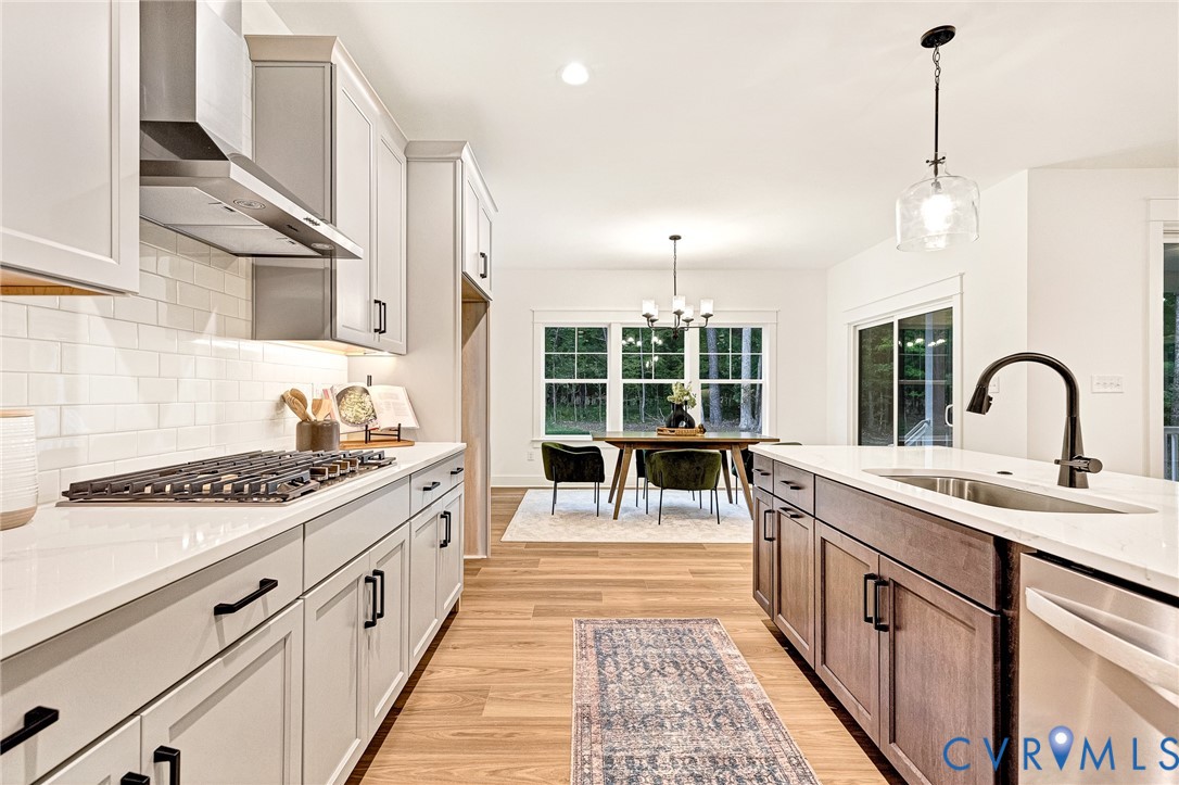 Kitchen featuring light-toned cabinetry, quartz countertops, subway tile backsplash, stainless steel gas cooktop with range hood, and a center island with under-mount sink and matte black fixture