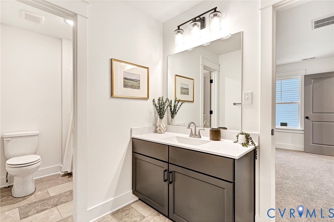 Bathroom featuring a vanity with dark cabinetry, white solid-surface countertop, rectangular undermount sink, and three-light wall-mounted fixture