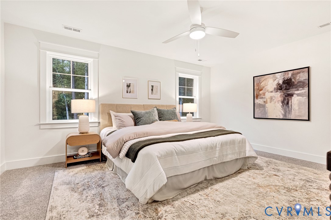 Bright room featuring neutral wall color, plush carpeting, double-hung windows with exterior trim, and a white ceiling fan with an integrated light fixture