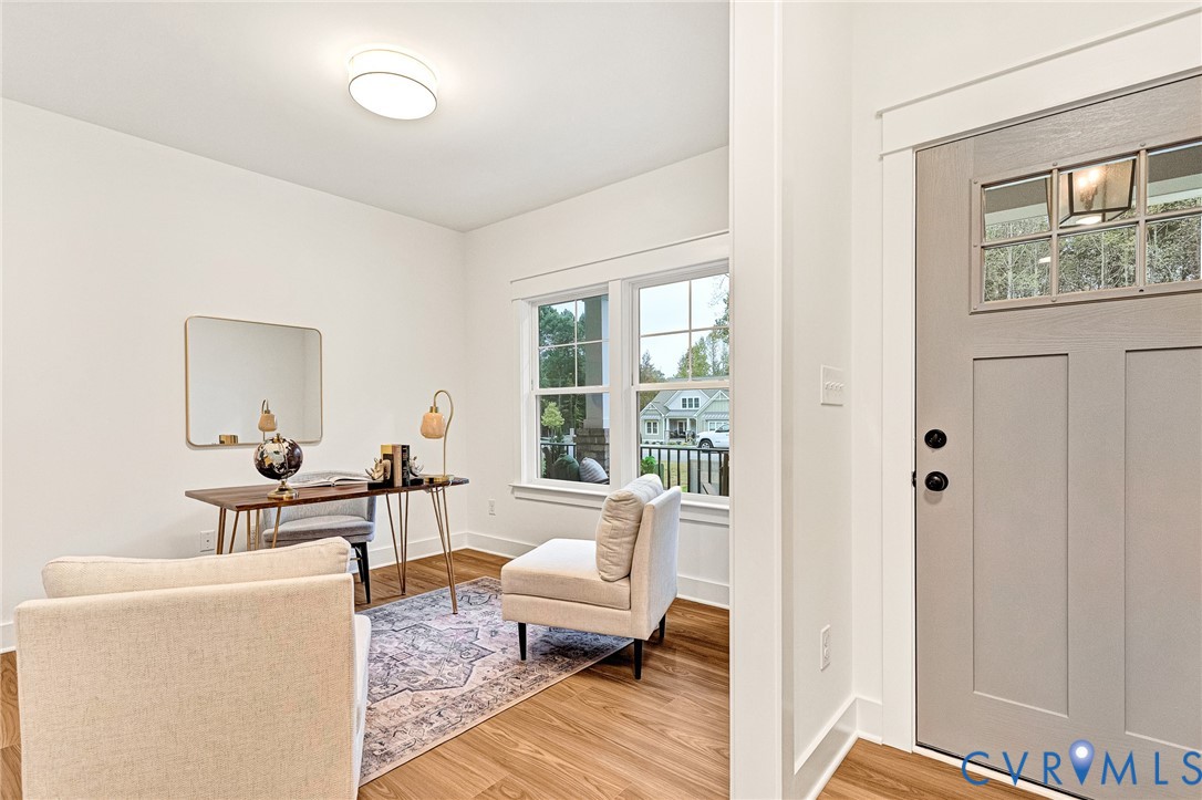 Neutral-toned solid core door with a multi-pane glass insert, wood-finish flooring, crisp white wall trim, and multi-pane windows with detailed framing