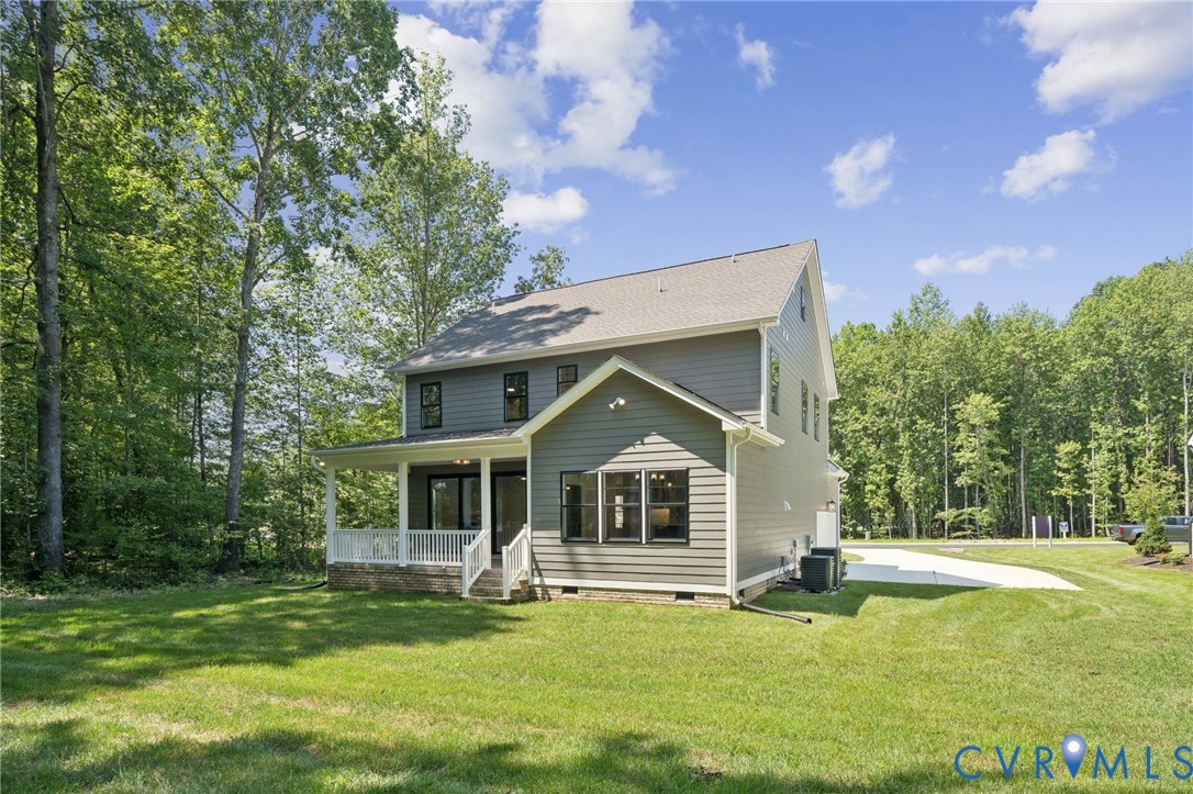 Two-story residence featuring grey lap siding, a covered porch with white railing, and a concrete driveway, situated on a lot with mature perimeter trees