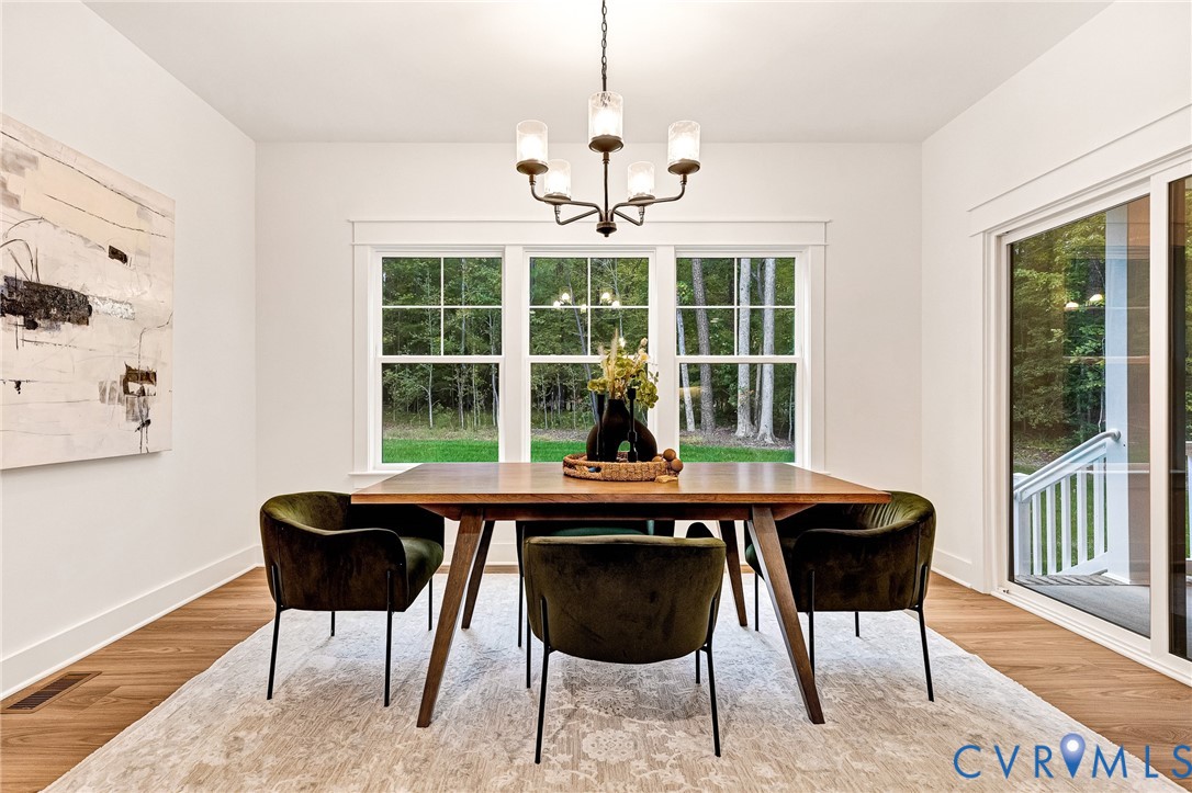 Dining space featuring wood-finish flooring, a multi-light metal chandelier with glass shades, grid-patterned windows, and a large sliding glass door