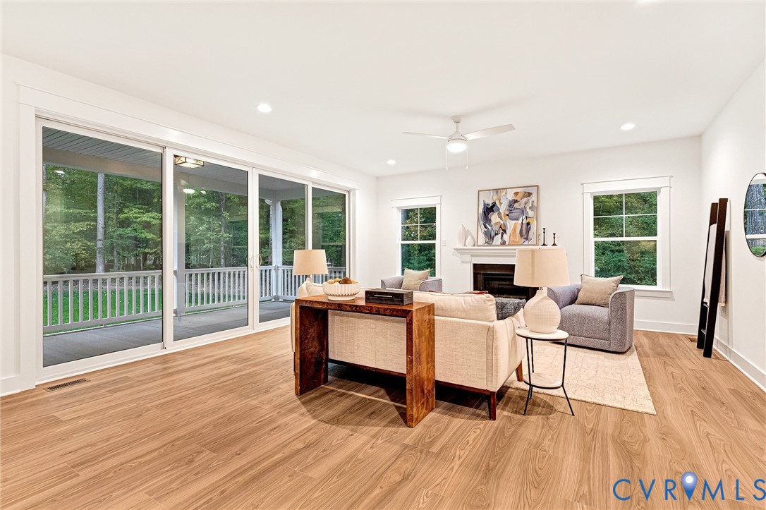 Living room featuring wood-finish flooring, a fireplace with a mantel, recessed lighting, a ceiling fan, and large sliding glass doors