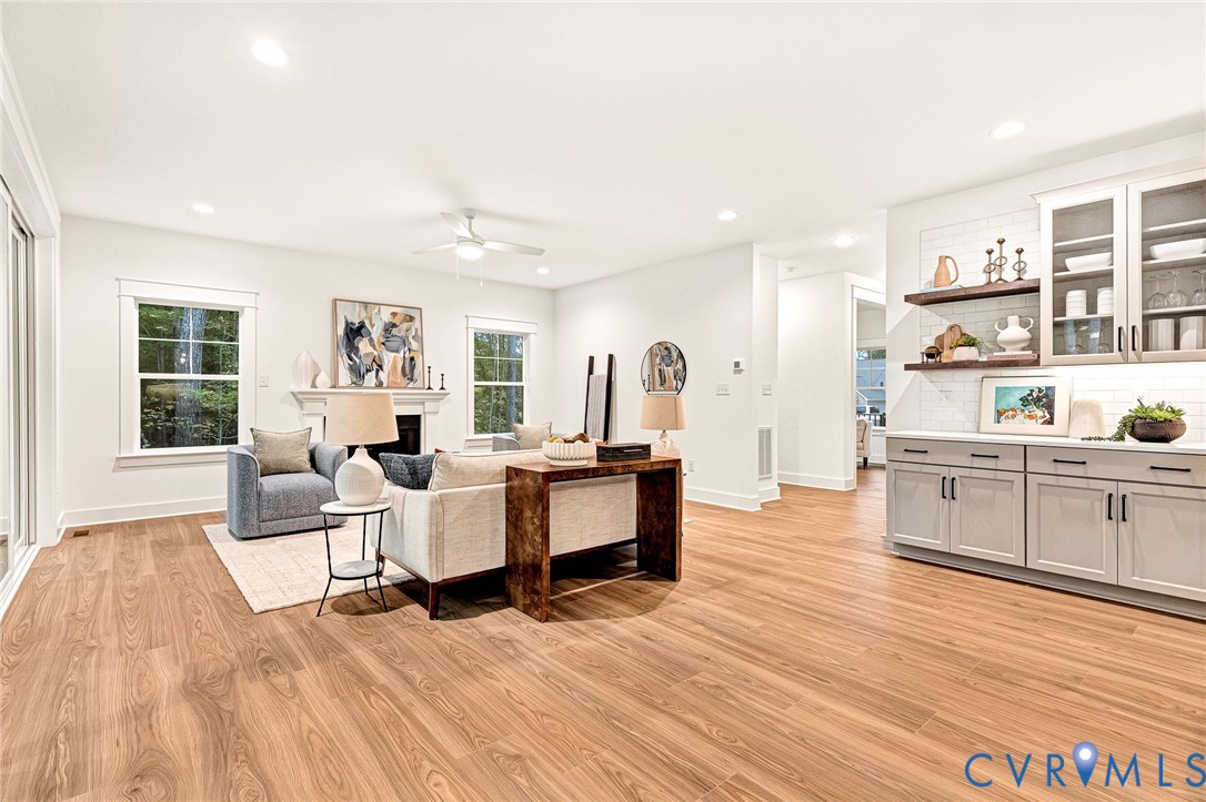Open-concept interior featuring wood-finish flooring, recessed lighting, a fireplace with a decorative mantel, and built-in cabinetry with glass-front uppers and floating wood shelves