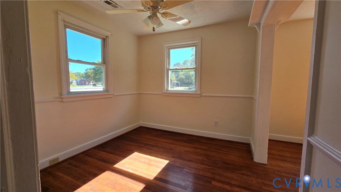 Room featuring dark-toned wood-finish flooring, white chair rail molding, dual windows with white trim, and a ceiling-mounted fan with integrated lighting Room featuring dark-toned wood-finish flooring, white chair rail molding, dual windows with white trim, and a ceiling-mounted fan with integrated lighting