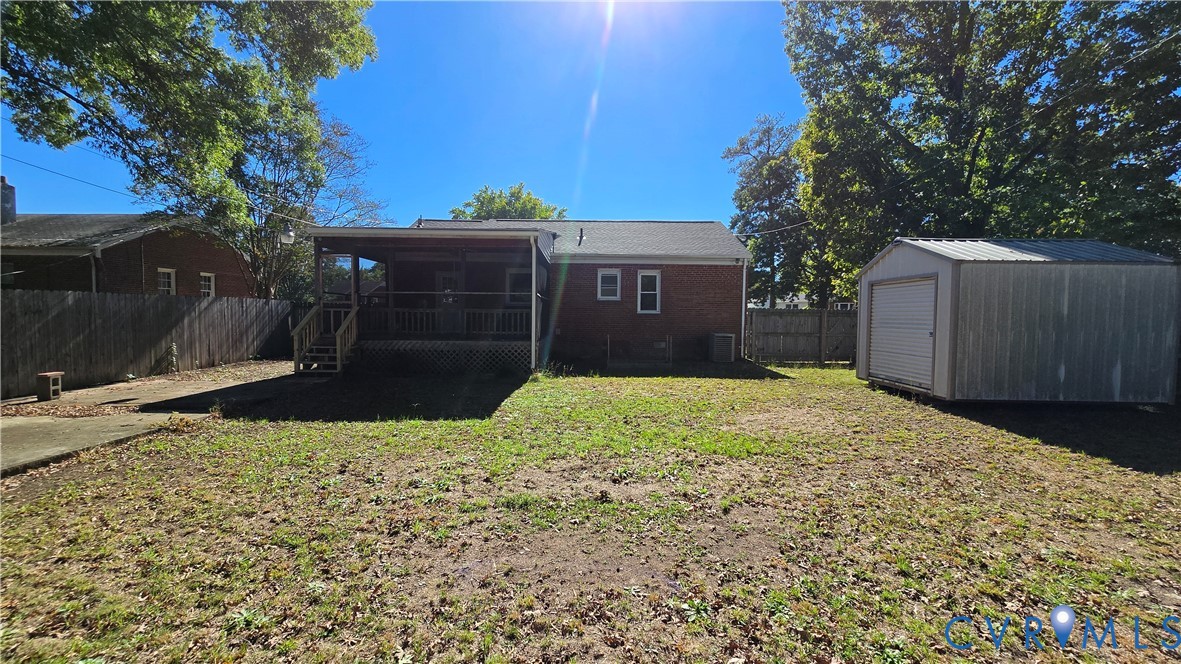 Rear exterior featuring a brick facade, covered wood deck, wood privacy fencing, and a detached metal storage building
