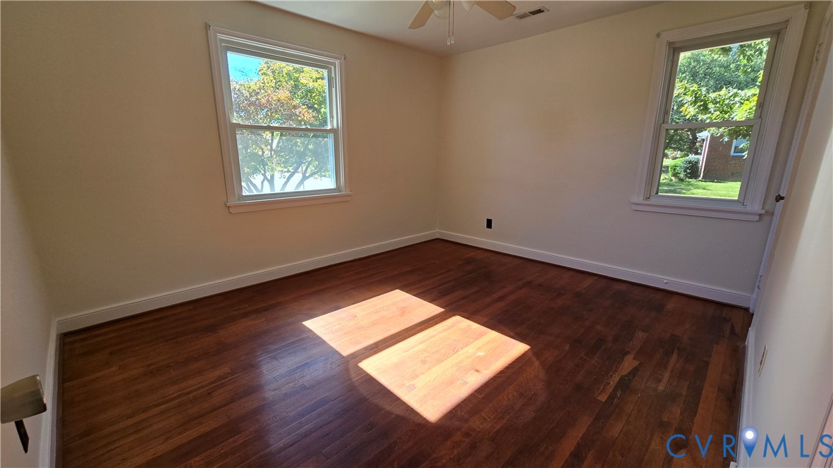 Room featuring wood-finish flooring, two windows with white trim, and a ceiling-mounted fan