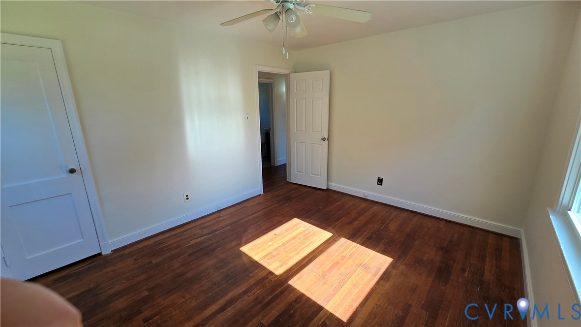 Interior room featuring wood-finish flooring, white paneled doors, and a ceiling-mounted light fixture with fan blades